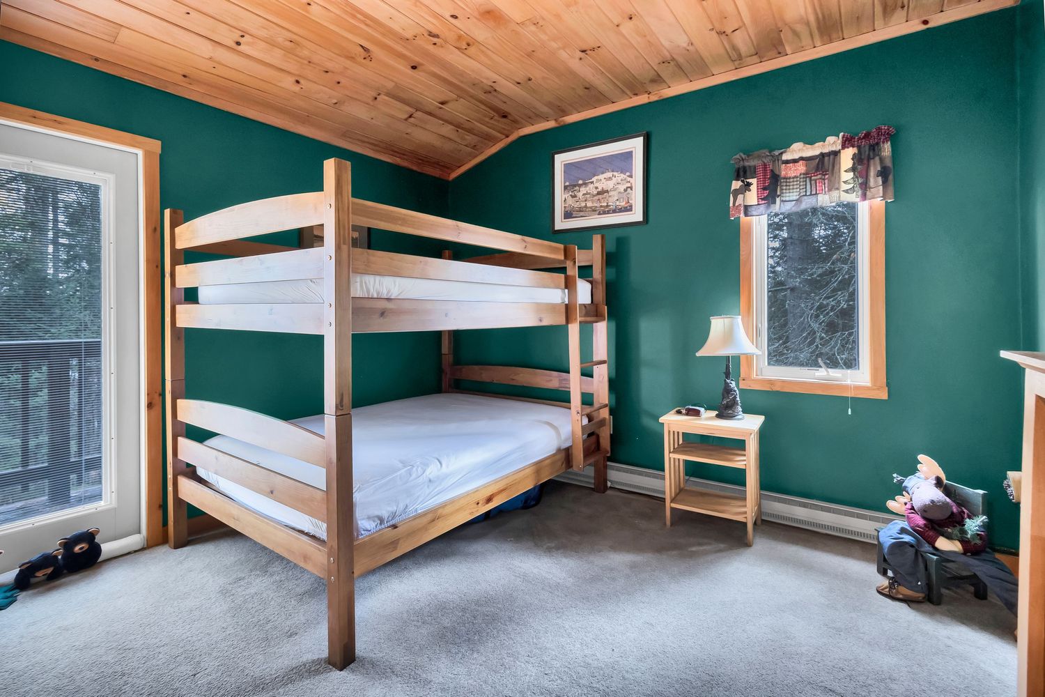 A rustic bedroom with wooden bunk beds, teal green walls, and a large window overlooking nature.