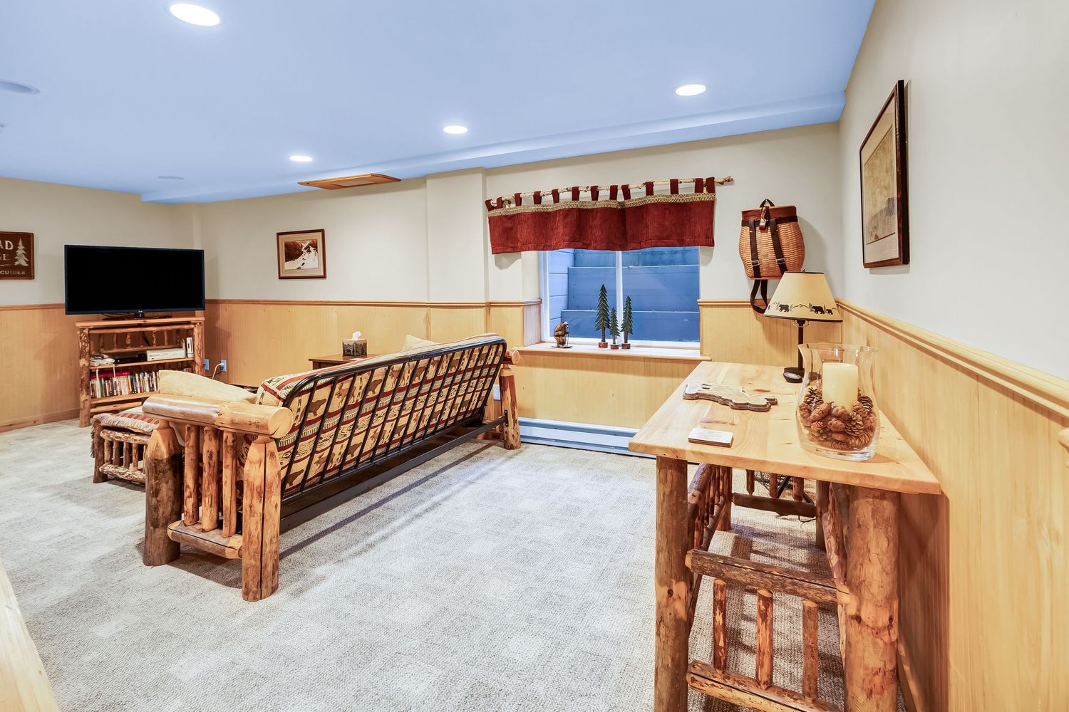 Rustic basement living room with log furniture, wood paneling, and a mounted TV features cozy cabin-style decor.