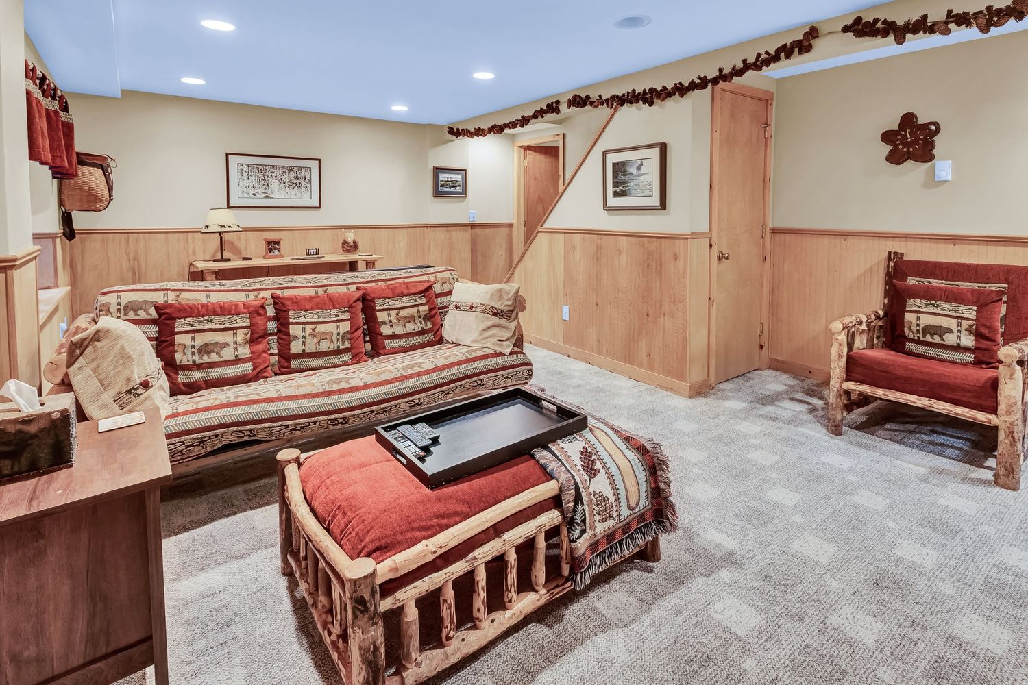 Rustic basement lounge area with wooden walls, red plaid cushioned benches and decorative garland trim.