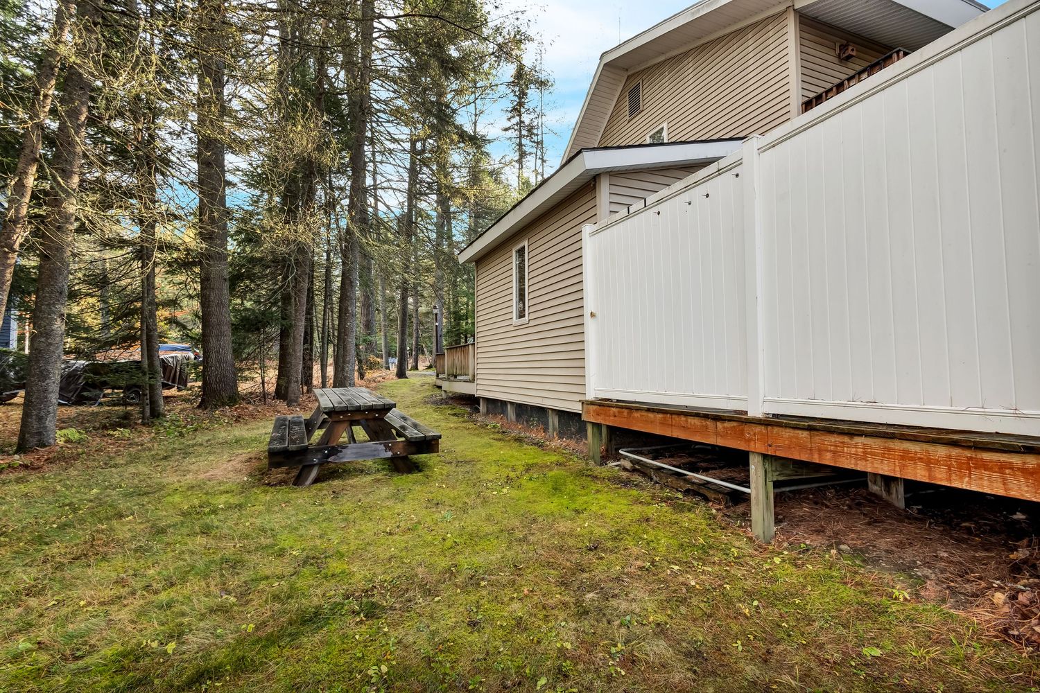 Exterior view of a beige modular home with wooden deck surrounded by tall pine trees.