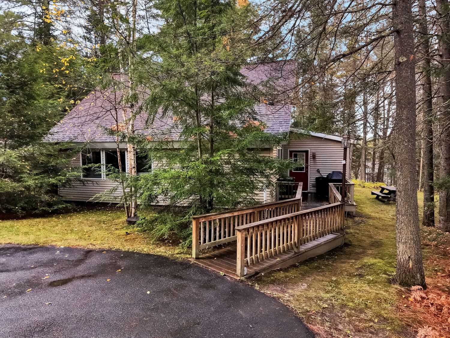 Woodland cottage with wooden ramp entrance surrounded by evergreen trees and fall foliage.