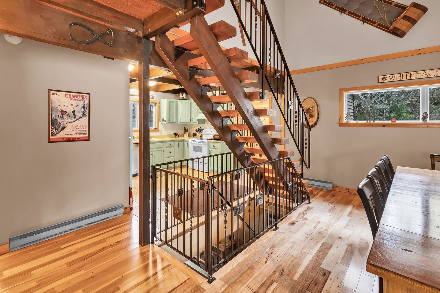 Modern staircase with wooden treads and black metal railings leads upstairs in an open concept home with hardwood floors.