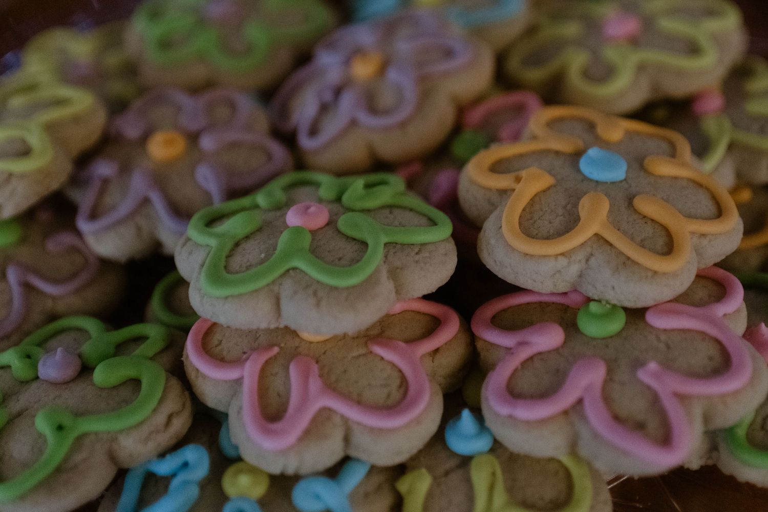 Colorful flower-shaped sugar cookies decorated with pink and blue icing and sprinkles arranged in rows.
