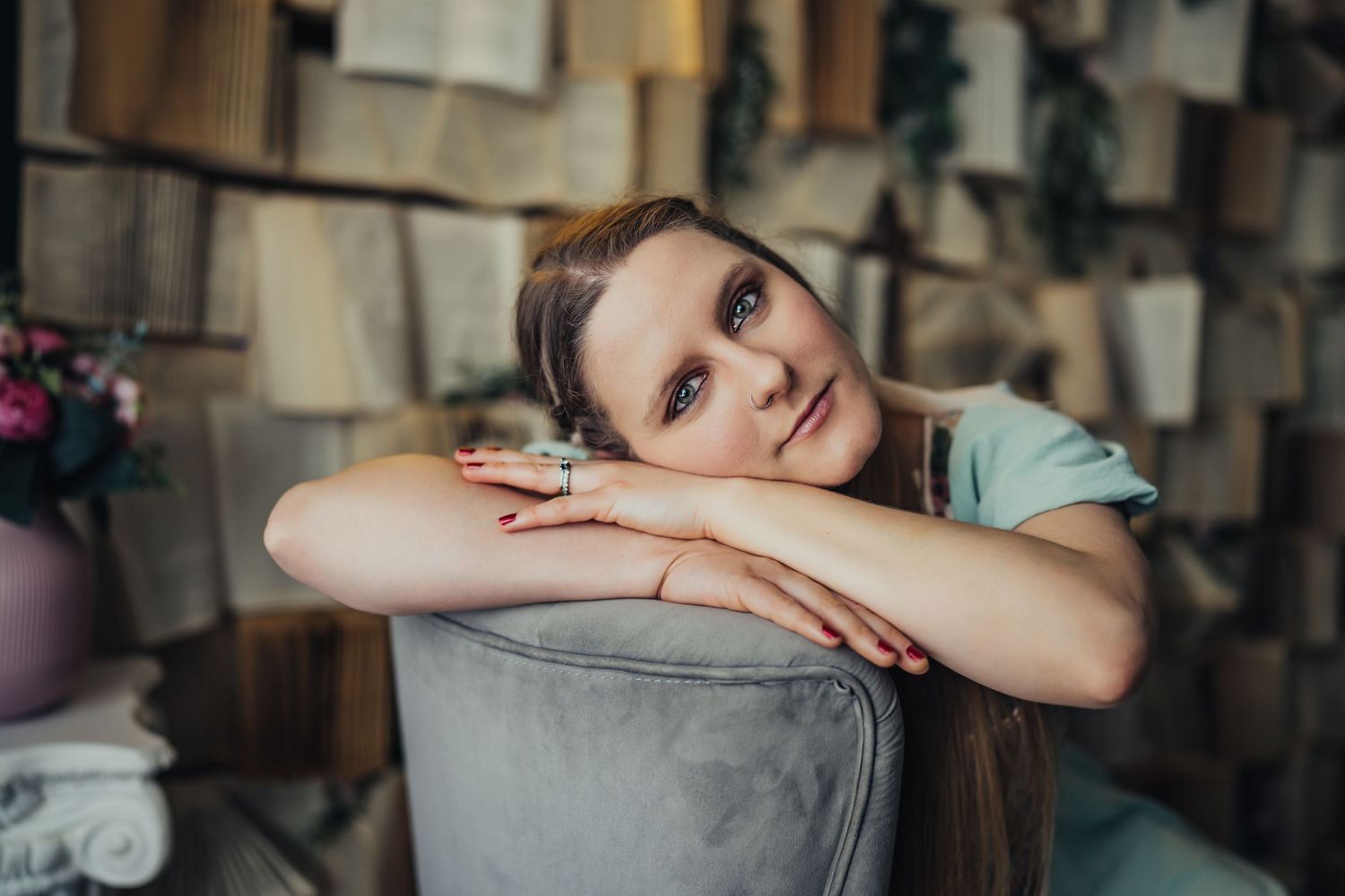 Young woman with long hair resting her chin on her arms over the back of a gray velvet chair.