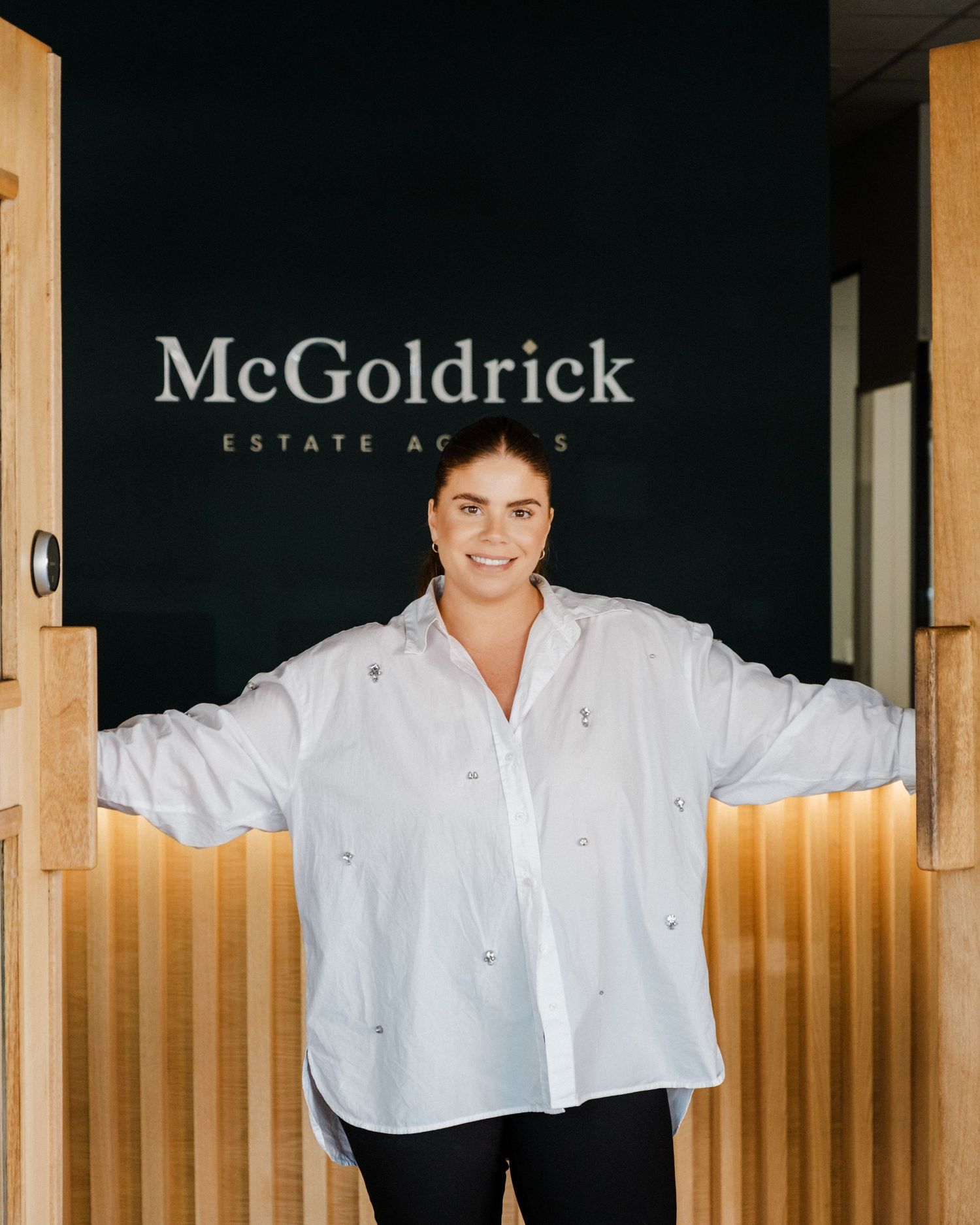 A person in a white button-down shirt stands in front of a wooden wall with McGoldrick signage visible.
