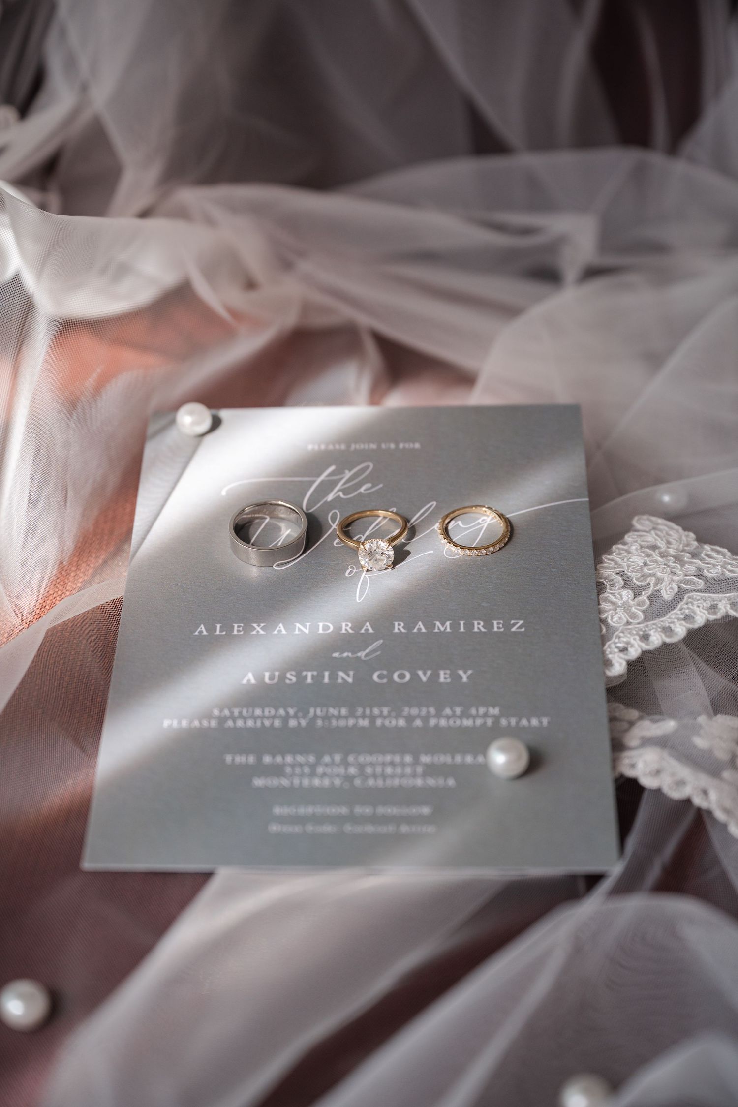 Elegant gray wedding invitations with silver text and rings displayed on delicate white lace and tulle fabric.