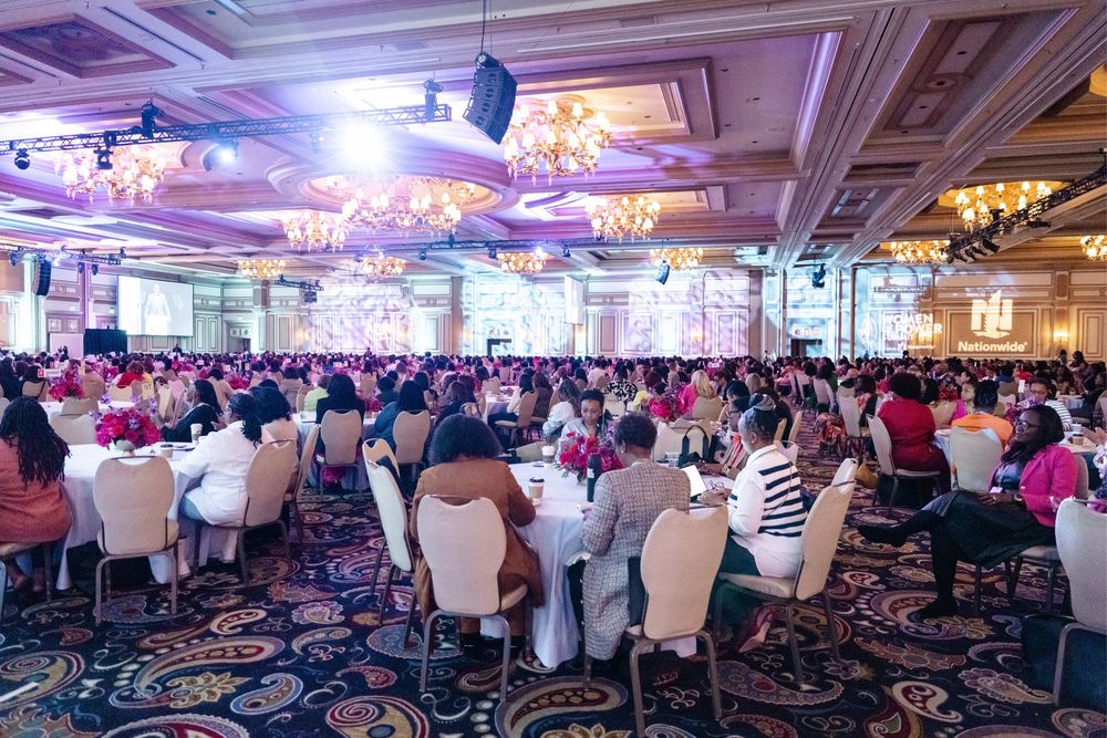 Elegant banquet hall with purple lighting, crystal chandeliers, and rows of tables set for a large formal event.