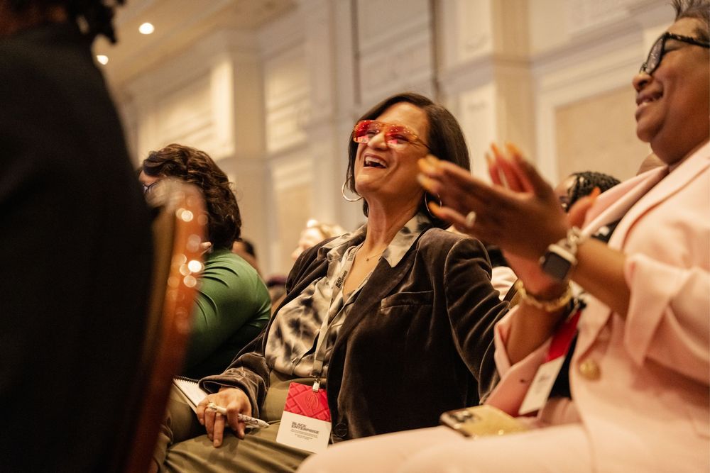 A group of people laughing and socializing at an indoor gathering with bright lighting.