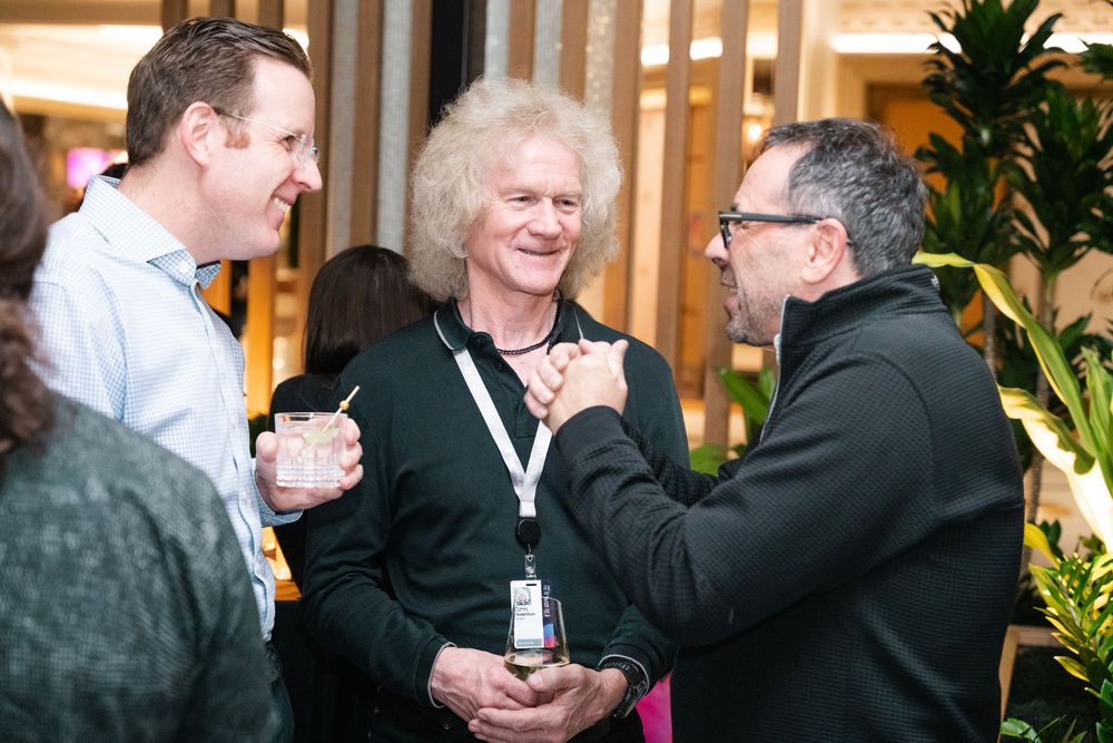 Two people share a warm embrace and laughter during a casual indoor gathering with plants in the background.