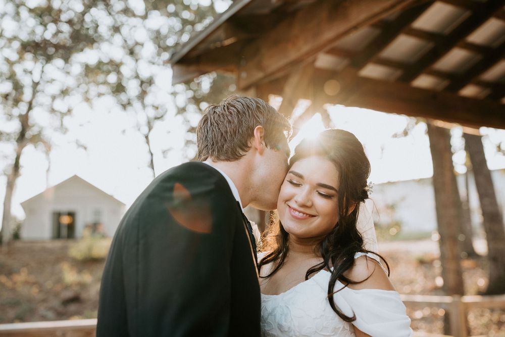 A couple shares an intimate moment under sunlit trees during a romantic outdoor photoshoot.