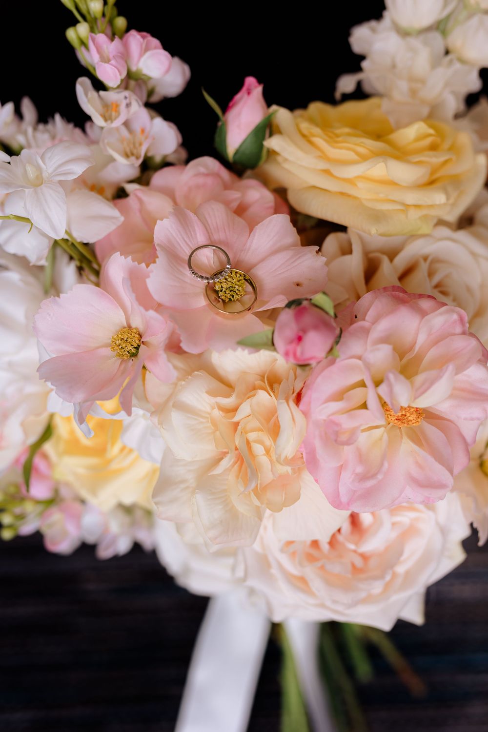 Delicate bouquet of pink and peach roses with a gold wedding ring nestled among the petals.