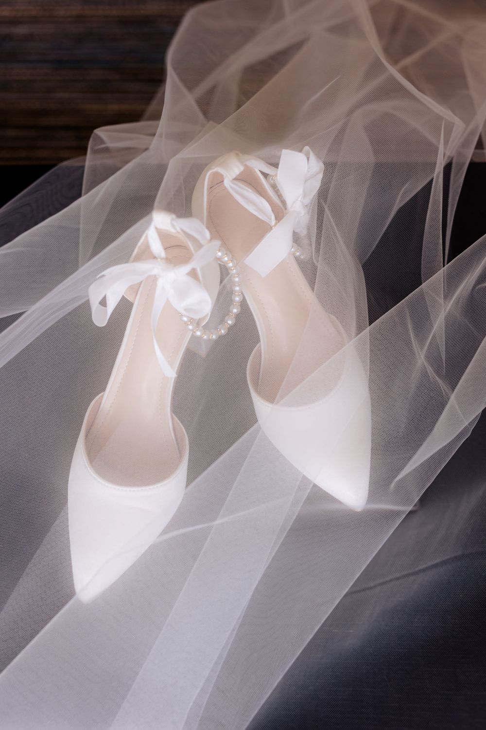 White bridal shoes with delicate veil overlay creating dreamy wedding detail shot.
