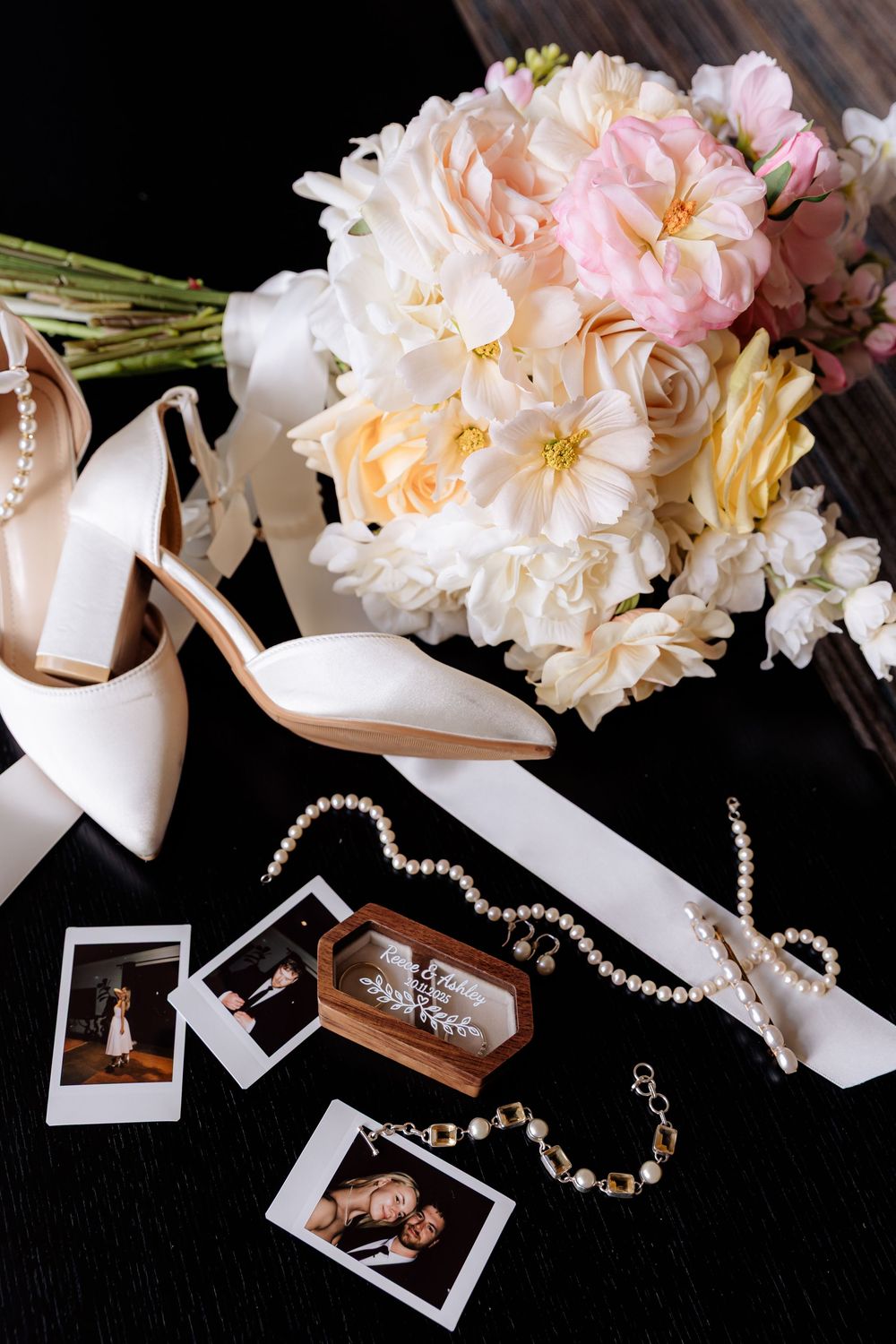 Wedding accessories including pearl necklaces, white ribbons, and delicate pink peonies arranged on dark background.