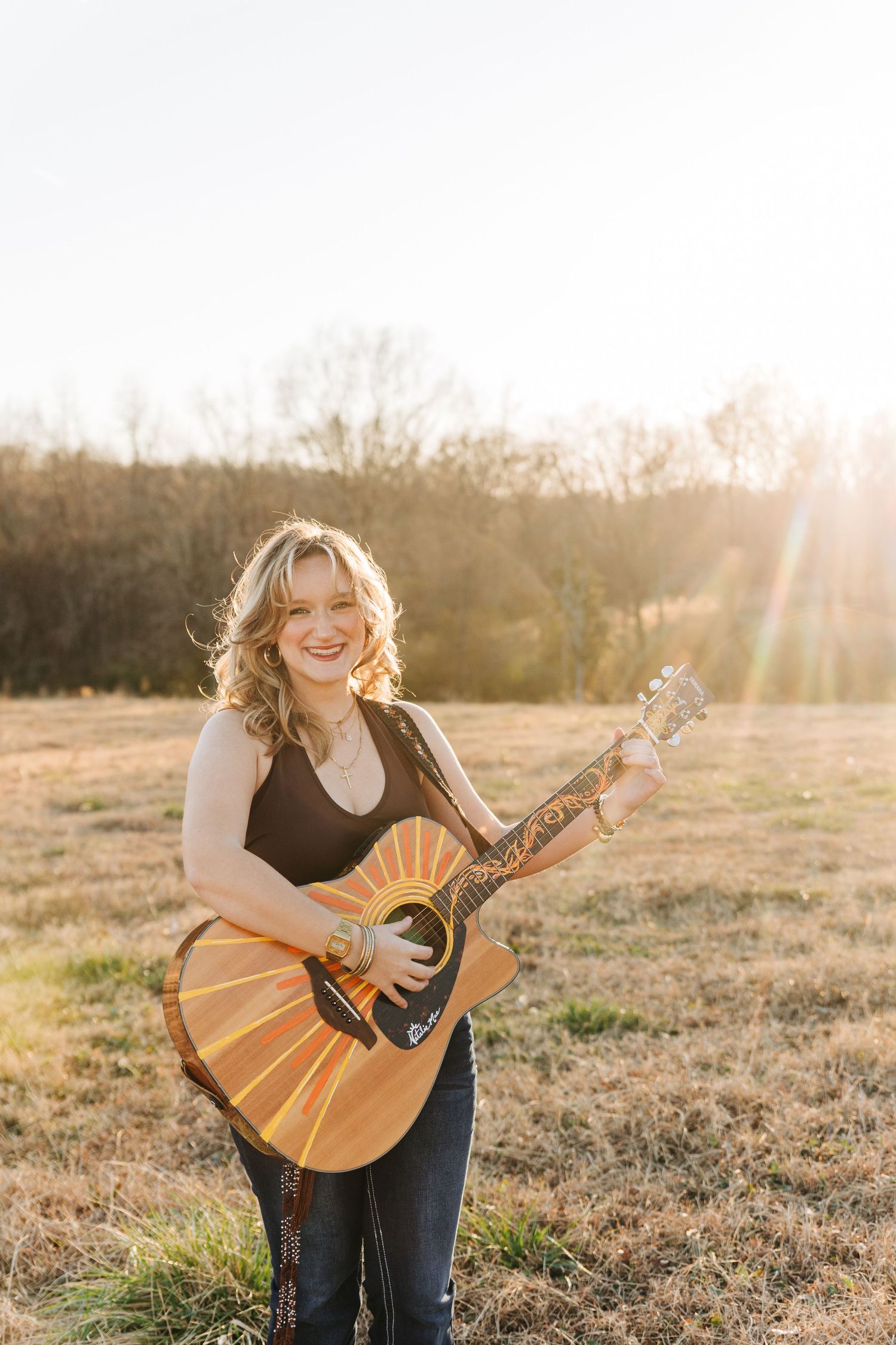 Musician playing acoustic guitar in golden sunlit field during sunset photoshoot series.