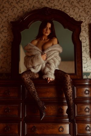Boudoir photo series showing figure in white fur and lace against ornate wooden furniture in moody lighting.