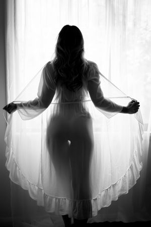 A silhouetted figure in white clothing stands against a bright backlit window in a dramatic black and white photo.