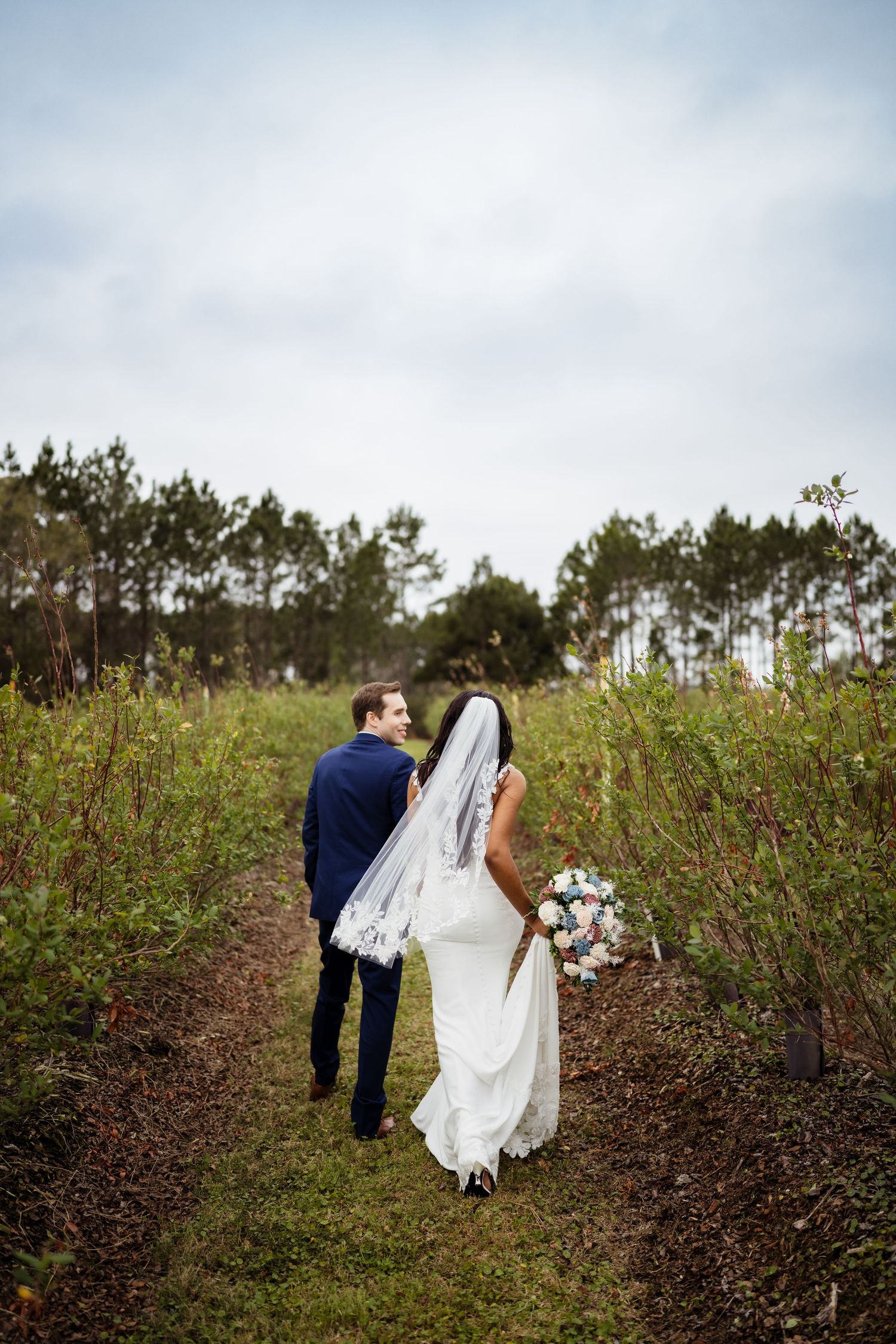 A bride and groom walk through a field of blooming wildflowers and bushes on their wedding day.