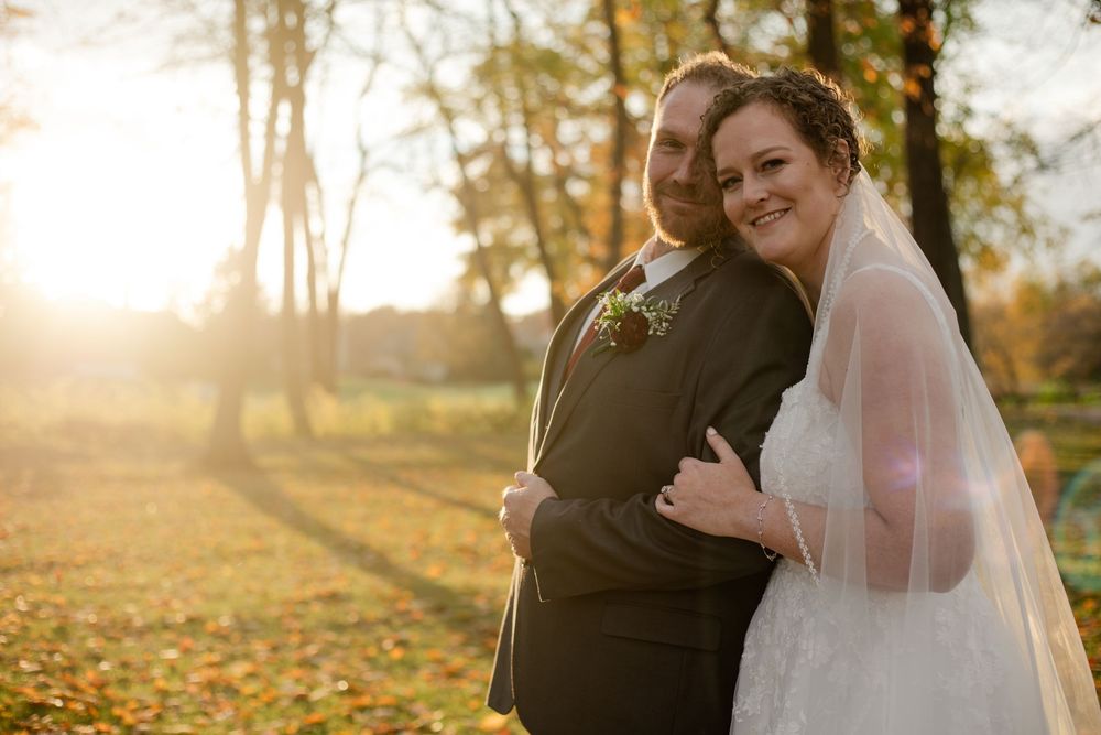 A romantic wedding couple embraces in a golden autumn setting during sunset.