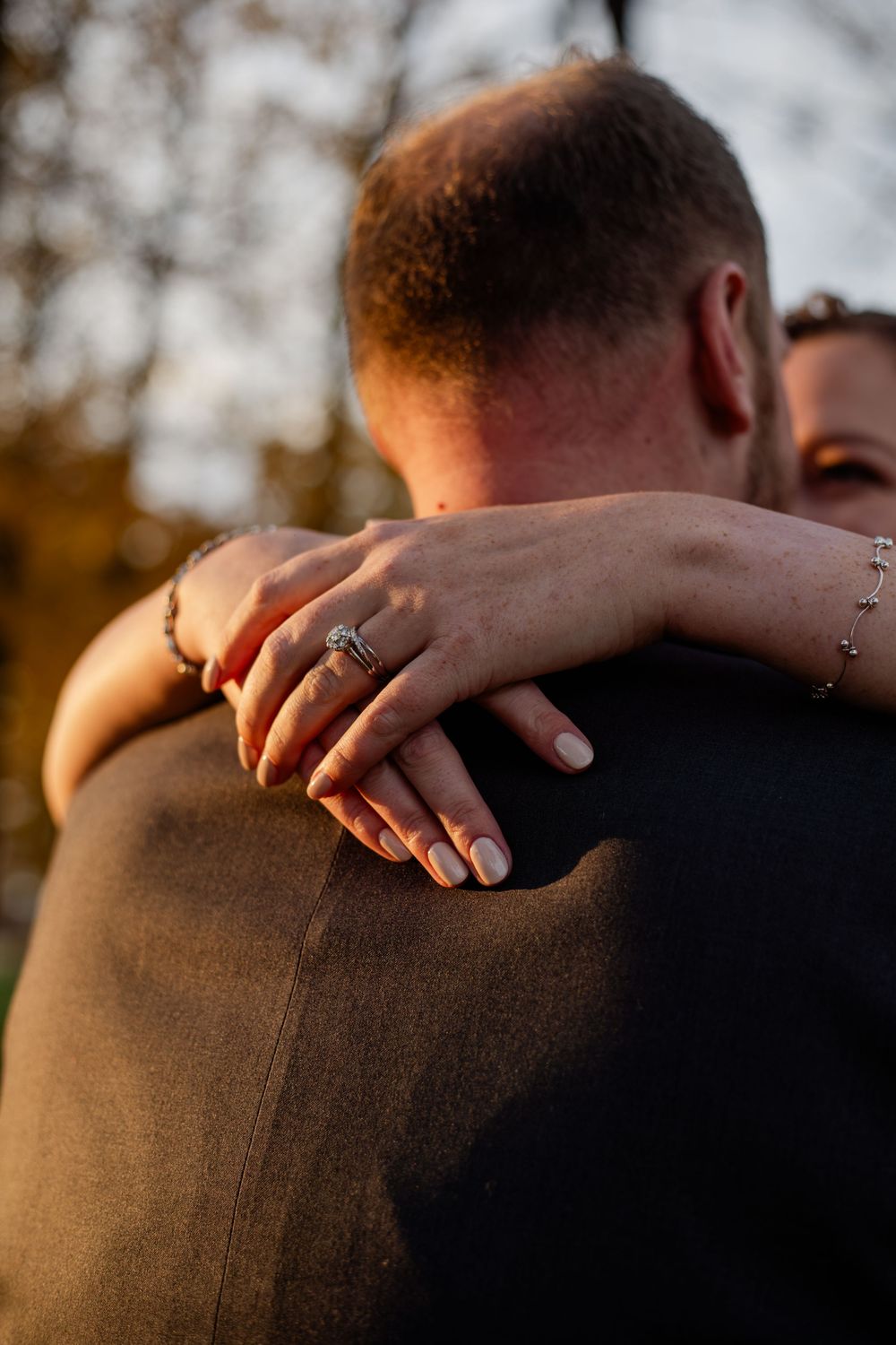 A close-up view of hands resting on shoulders during a romantic sunset moment.