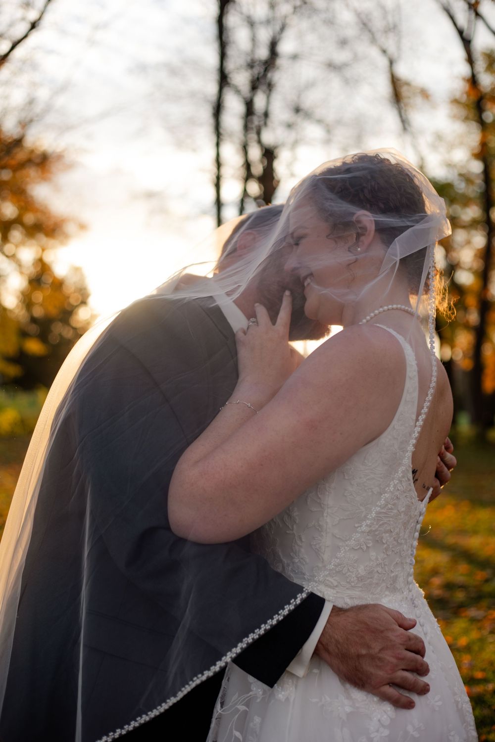 A romantic embrace captured in soft golden sunlight with a white wedding veil flowing.