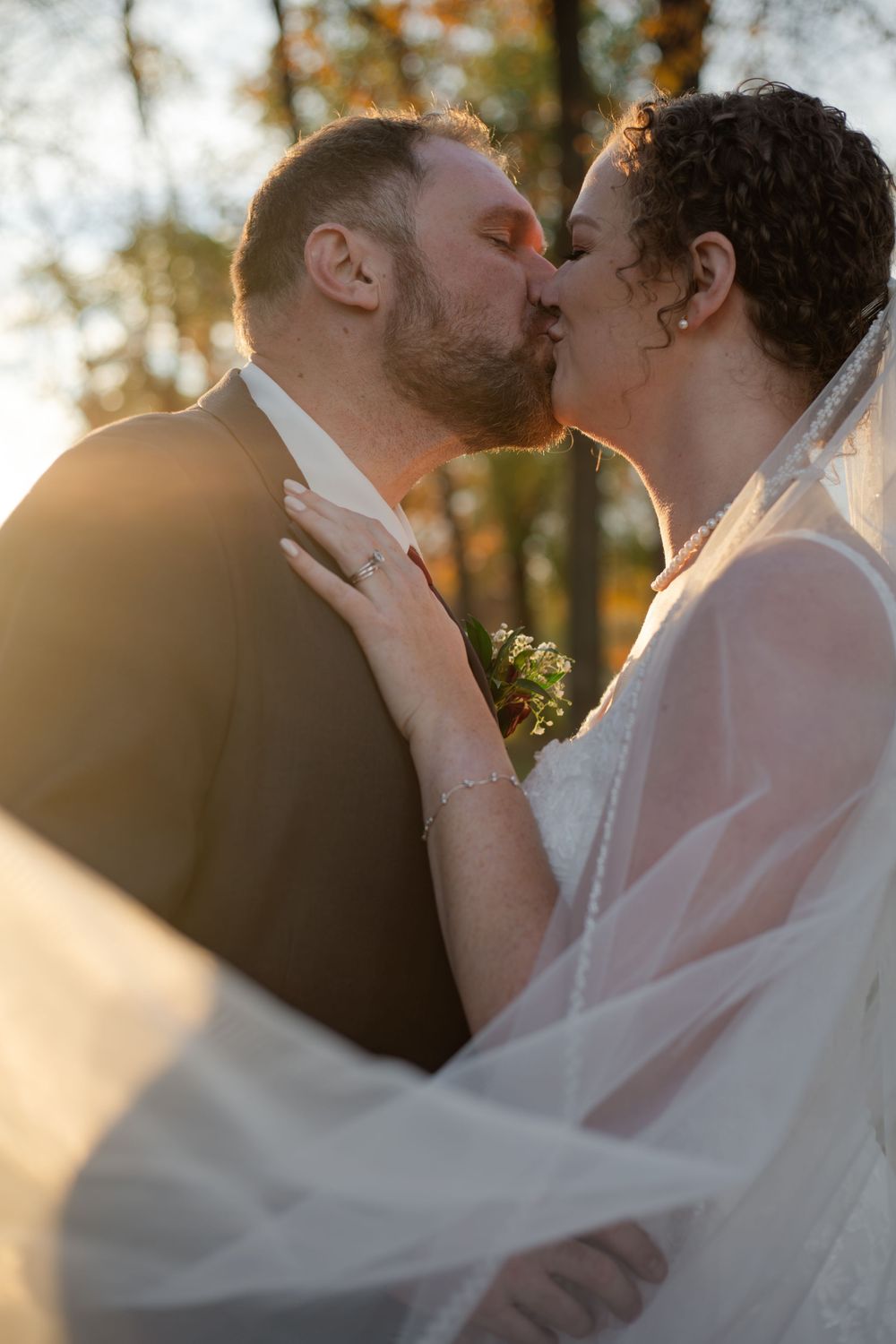 An intimate wedding kiss photographed through a delicate veil at sunset.