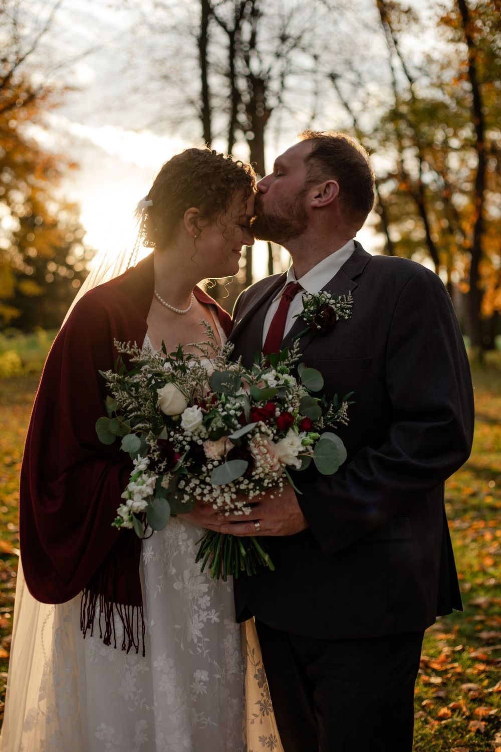Romantic autumn wedding couple shares tender moments in a forest setting with golden sunlight and fallen leaves.