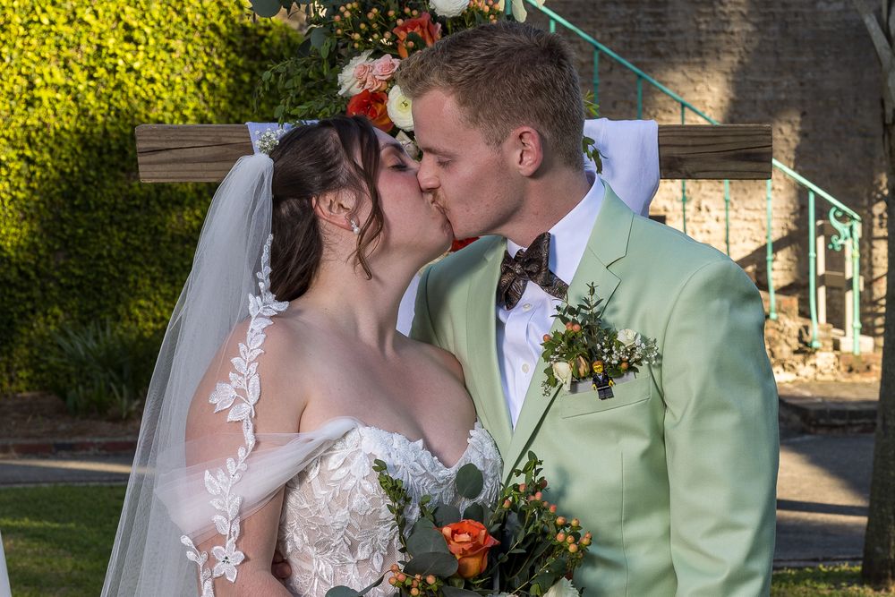 A romantic wedding moment with the bride in lace and groom in mint green suit sharing a kiss outdoors.