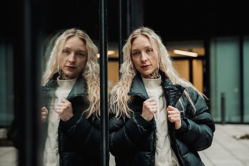 Person with long blonde hair wearing a black leather jacket poses in front of a window in a series of candid shots.