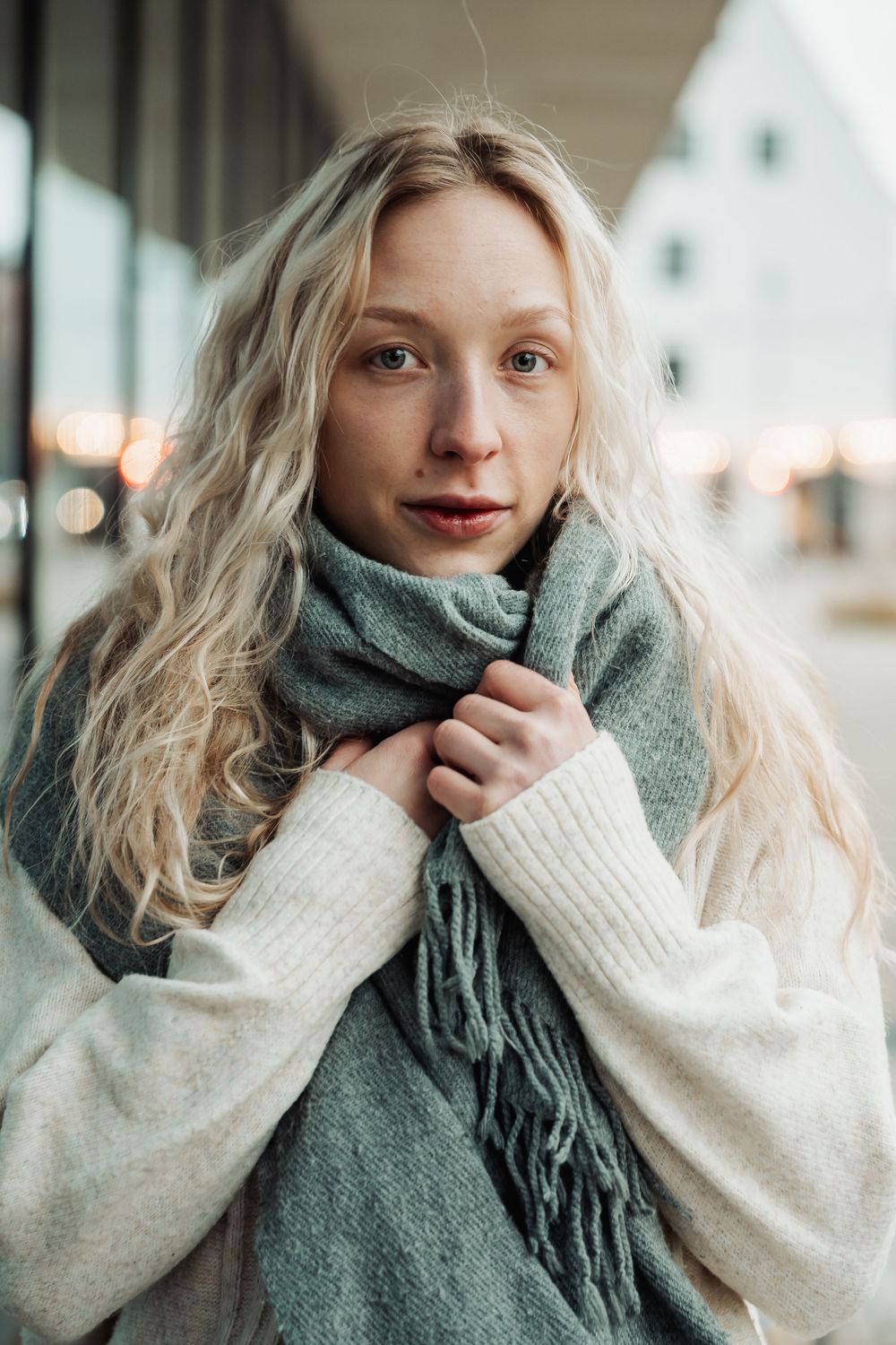 Portrait series showing winter fashion with cozy white sweater and green scarf against blurred background.