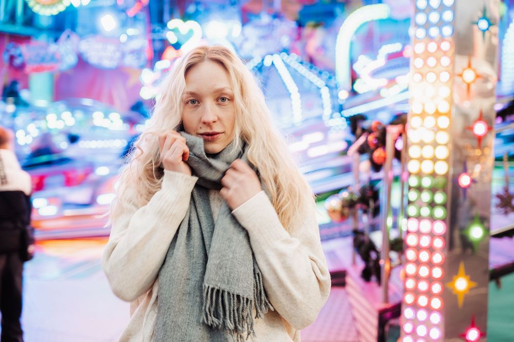 Person in a gray scarf poses playfully against colorful neon lights in an urban setting.