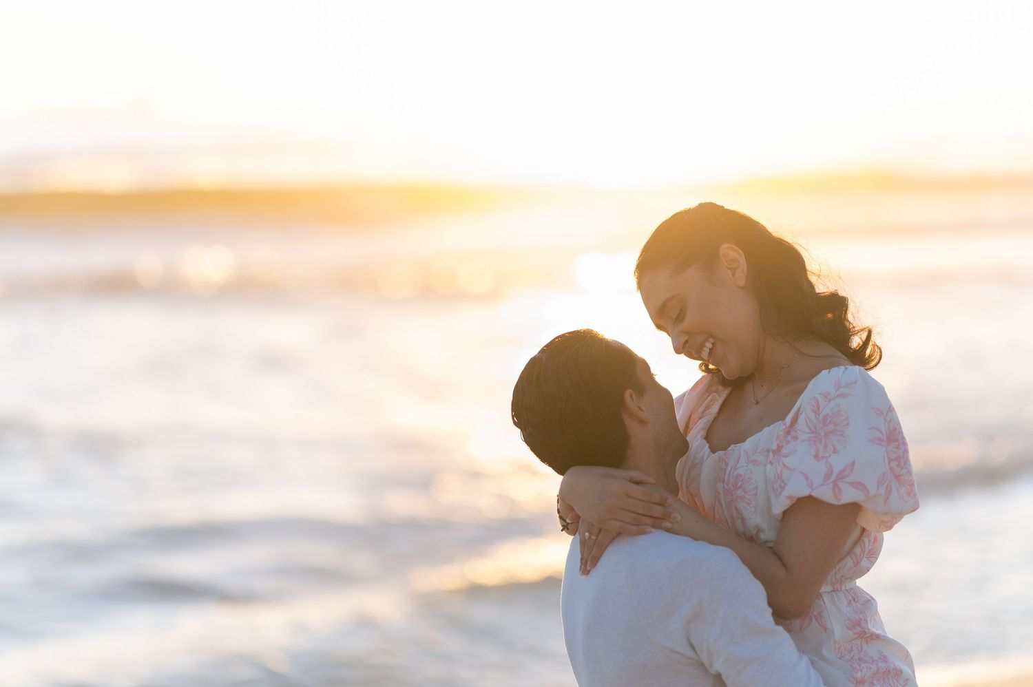Couple embracing romantically on a beach at golden sunset, waves in background.