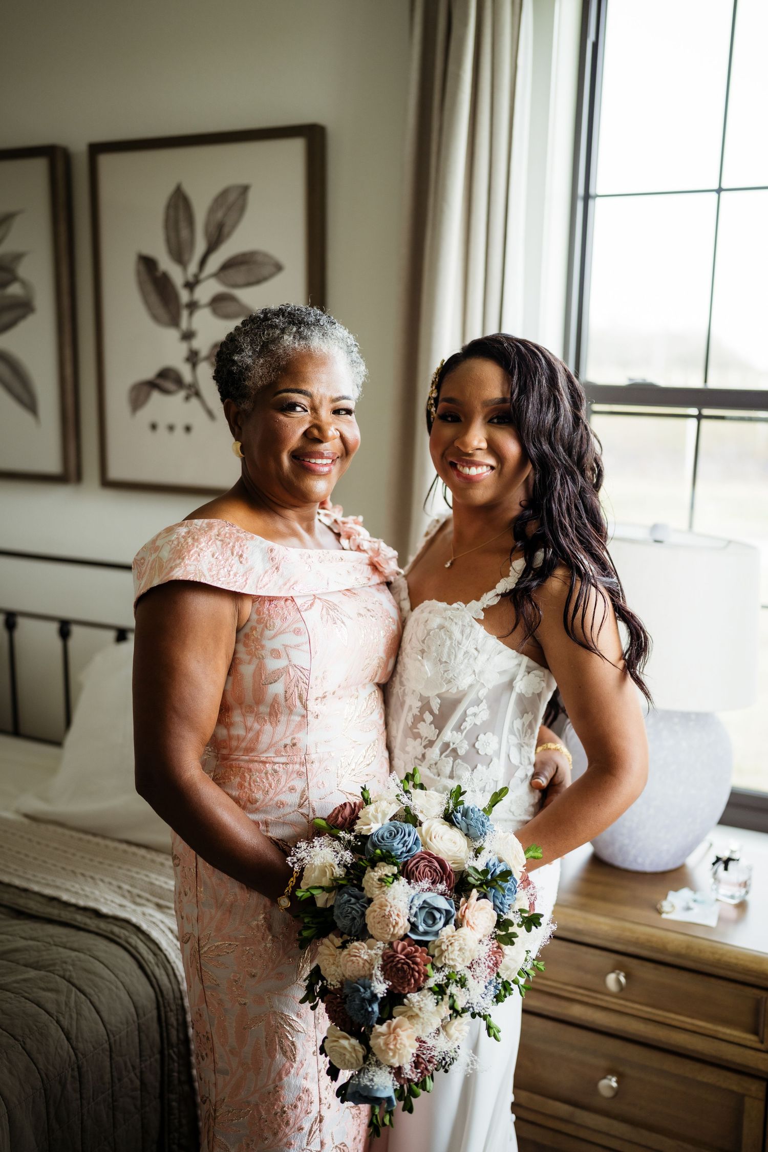 Two people share a tender moment in matching floral and white dresses while holding a beautiful blue and white bouquet.