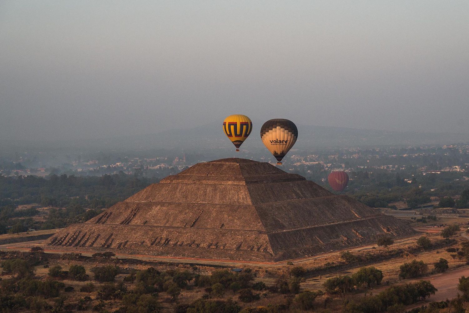 Hot air balloons float above the ancient Pyramid of the Sun in Teotihuacan, Mexico during a misty morning.