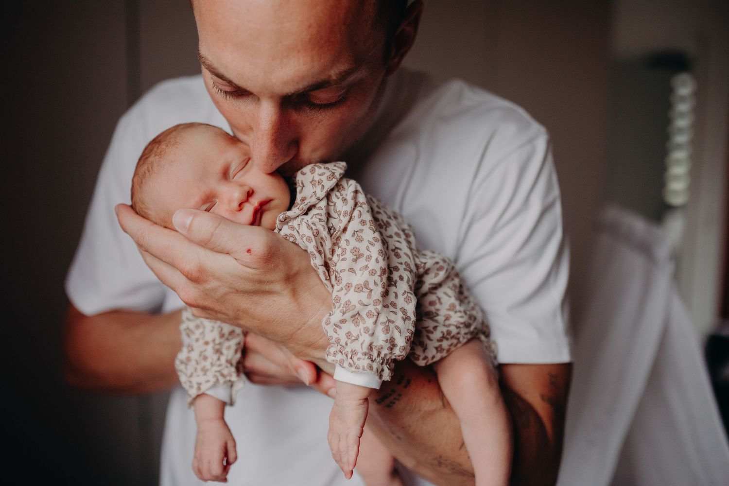 Loving father kisses his sleeping newborn baby in a tender close-up portrait.