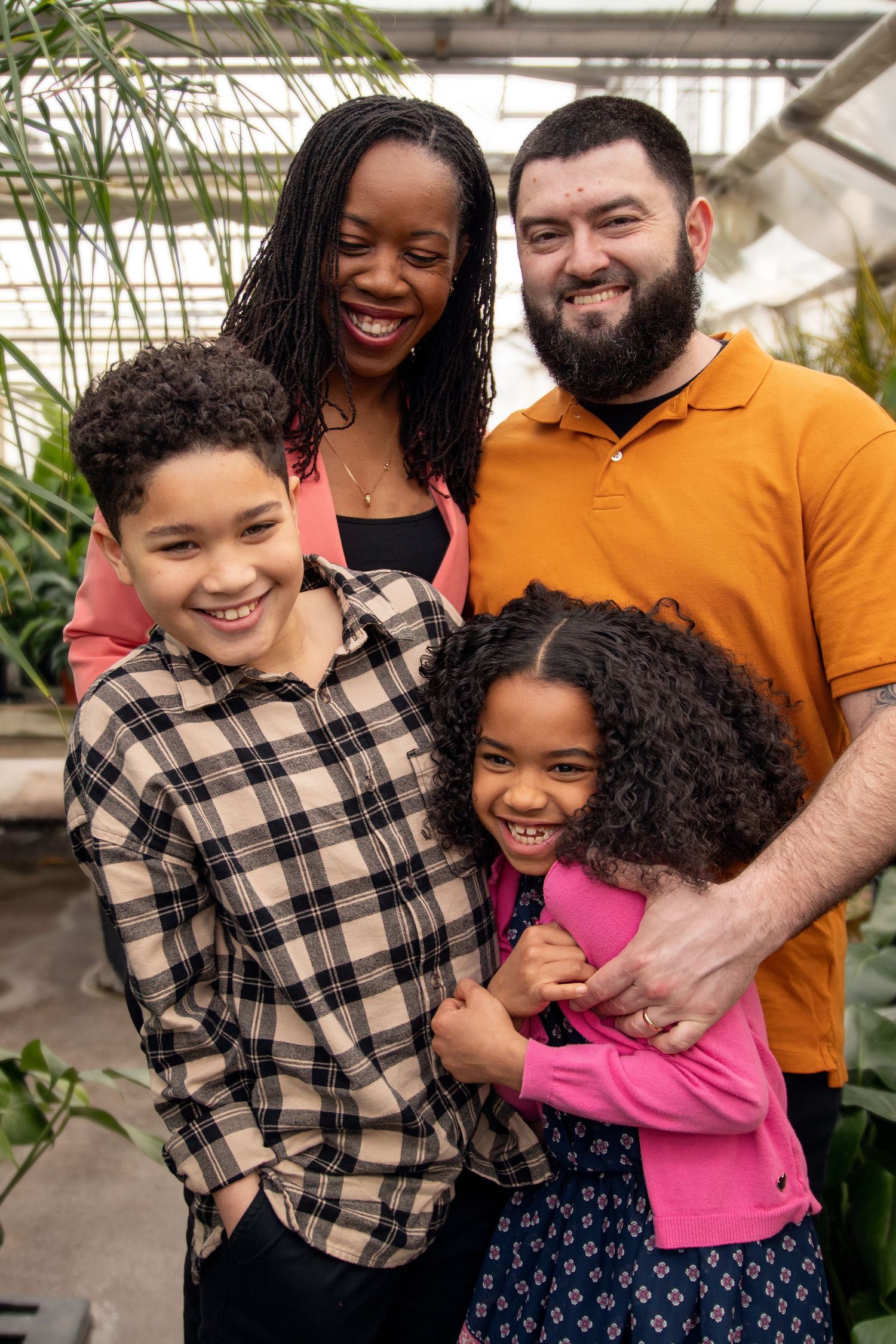 A happy family laughing and embracing together in a greenhouse setting with natural light.