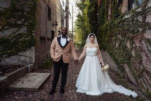 Wedding couple poses in front of ivy-covered brick wall for romantic outdoor photo series.
