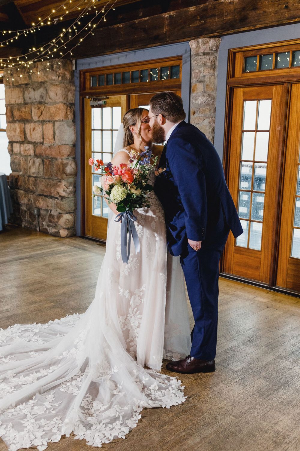 Elegant wedding couple shares intimate moments in a rustic stone venue with wooden windows and twinkling lights.