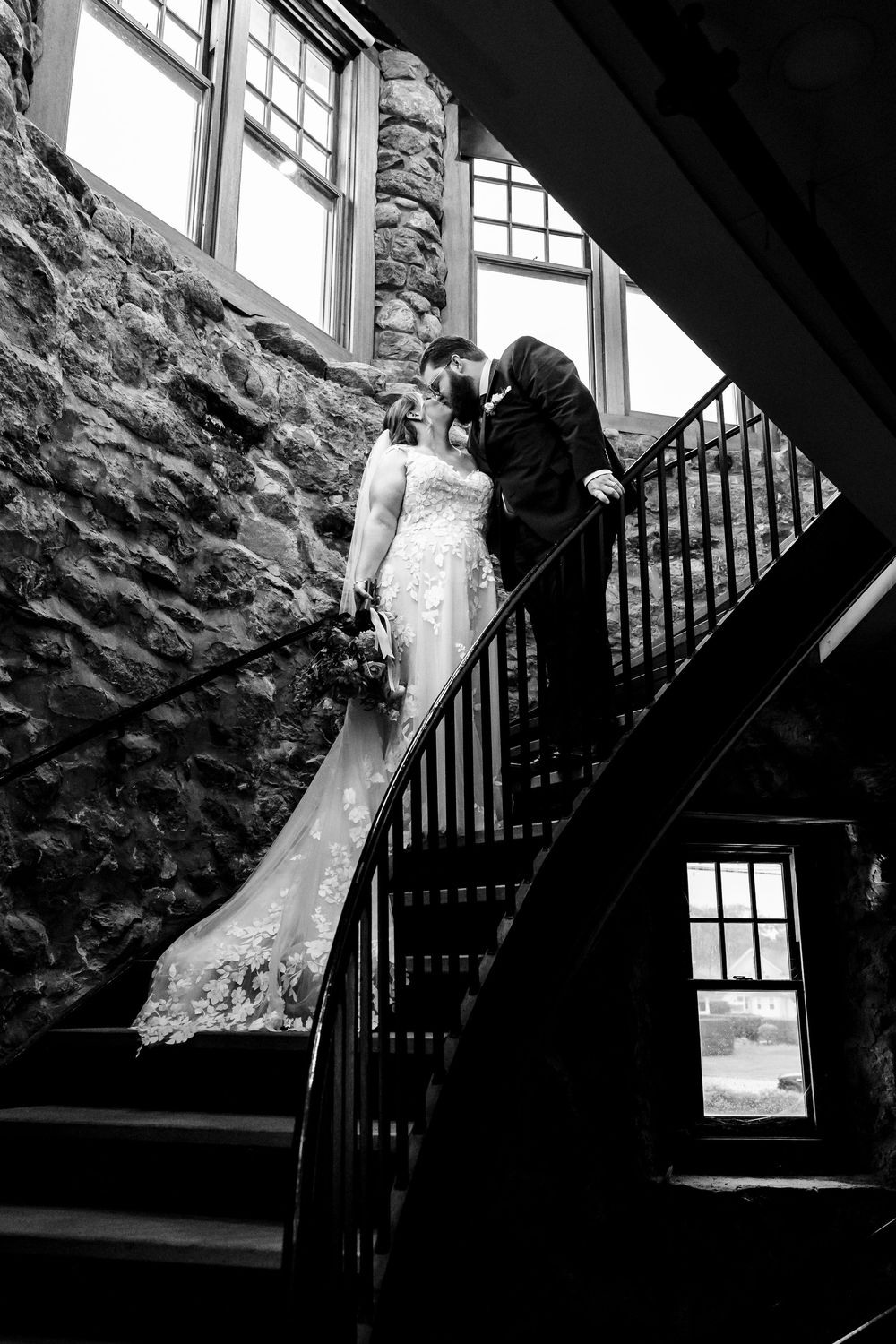 Black and white wedding photograph capturing dramatic angles on rustic stone staircase with natural window light.