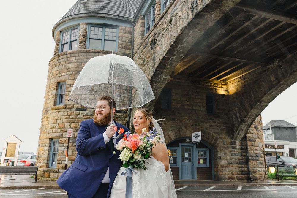 Wedding couple stands beneath a stone archway during a rainy day photoshoot.