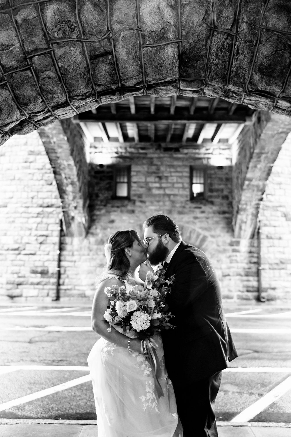 Black and white photo of a couple sharing an intimate moment under a brick archway.