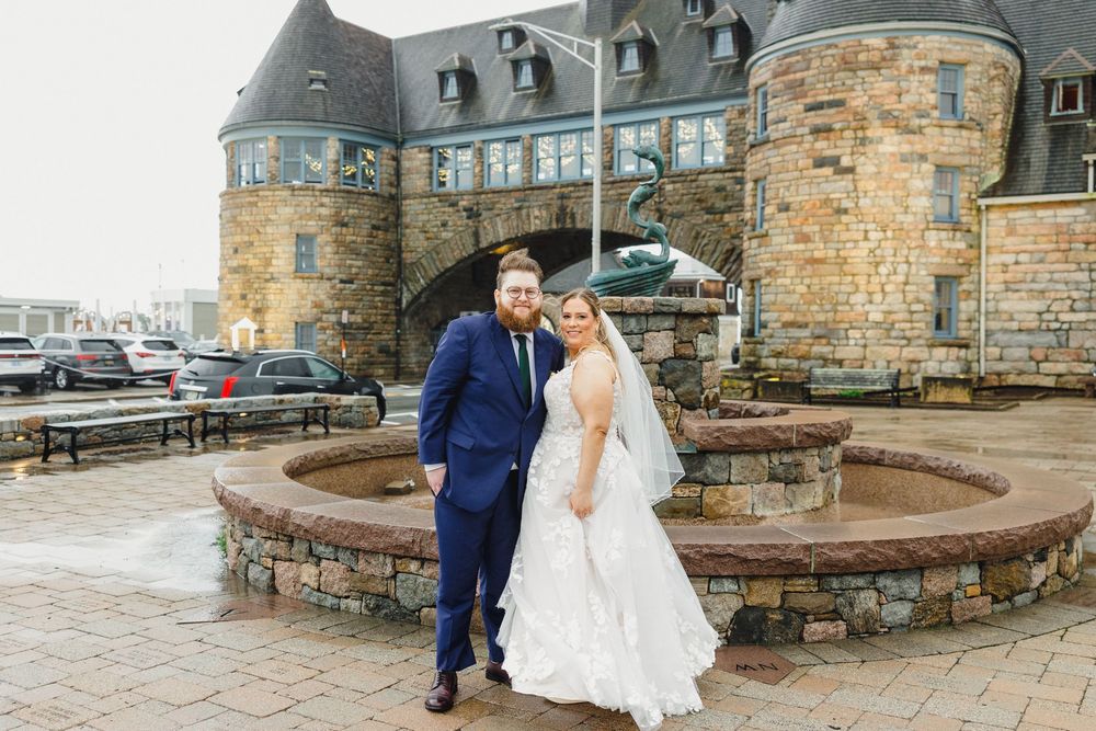 Newlyweds pose together on a stone patio outside a historic castle-like building.
