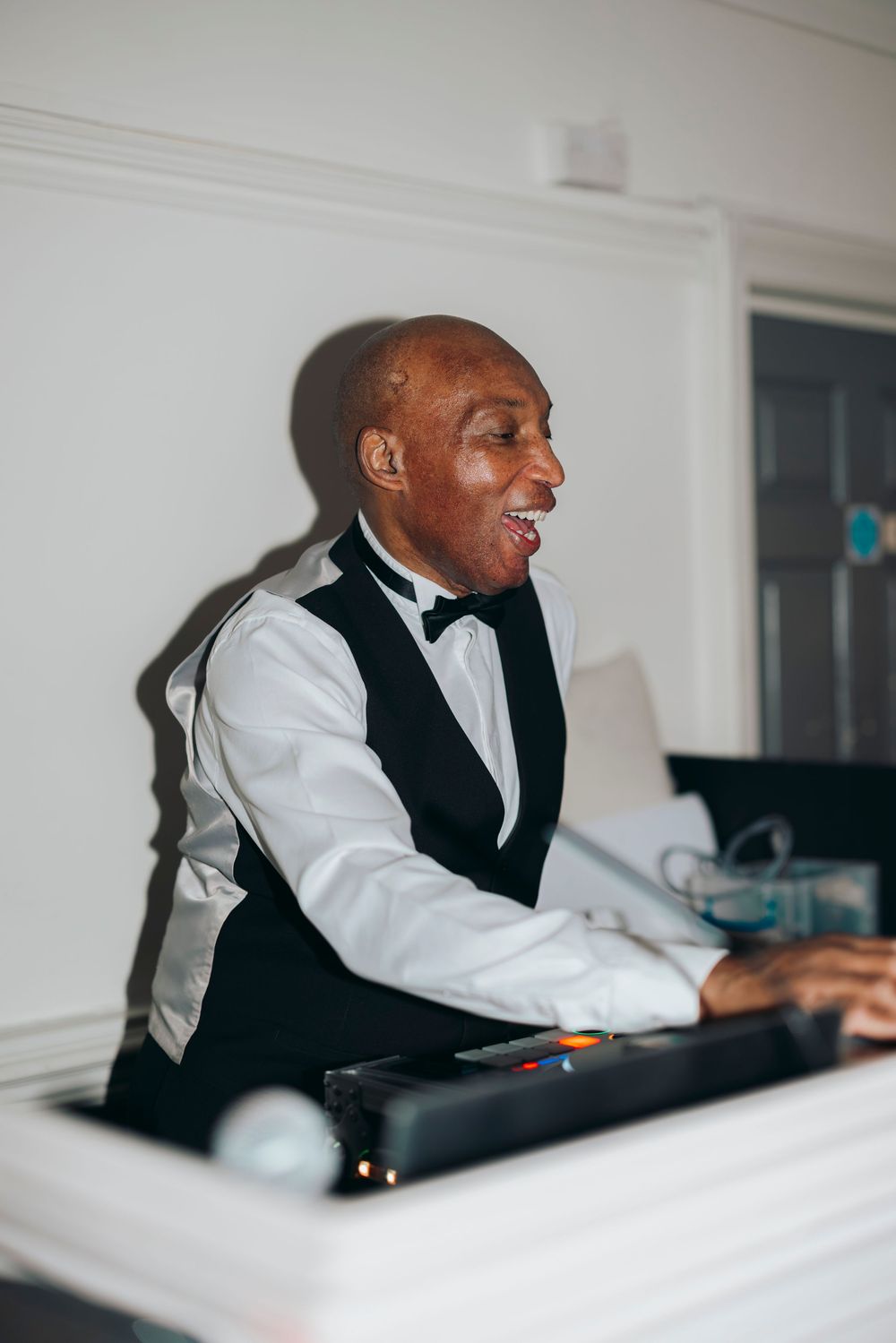 A musician in formal attire plays piano passionately while performing in a bright white room.