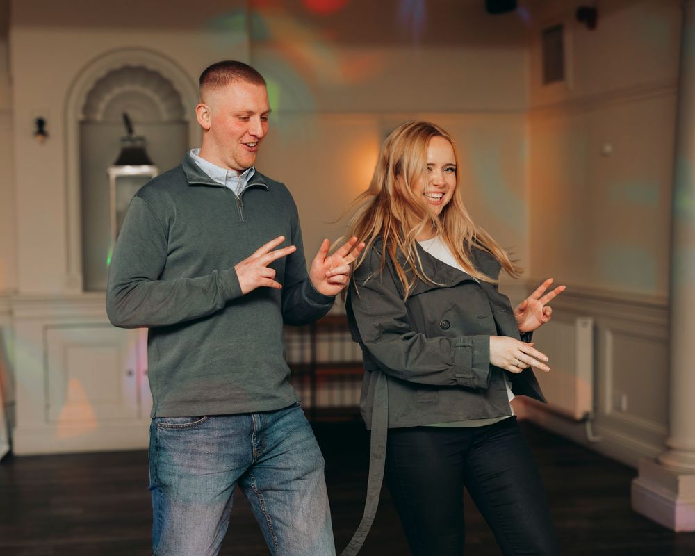 A couple dances together in a dimly lit room, showing playful movement and joy during their dance session.