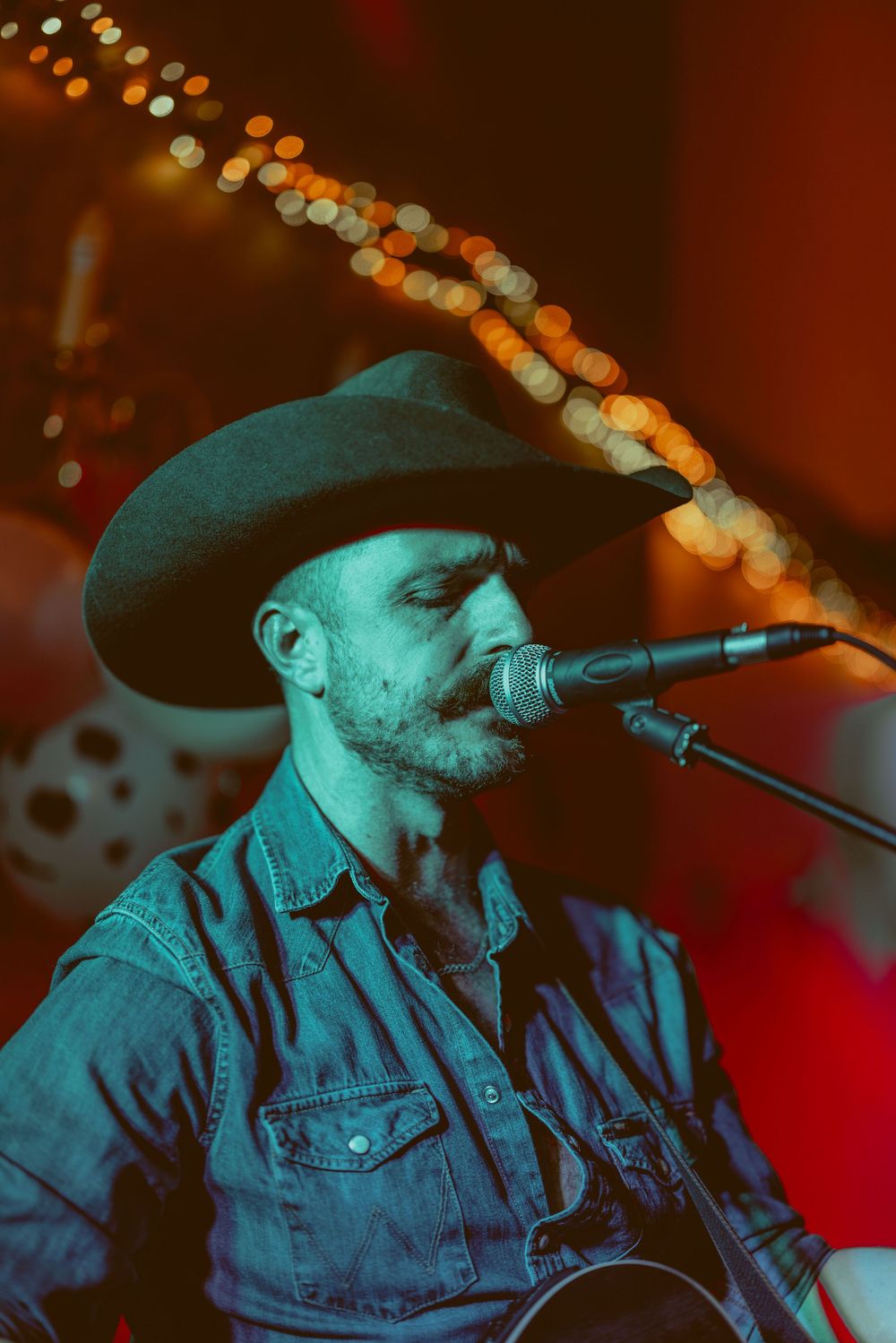 A musician in a denim jacket performs on stage under moody blue lighting.