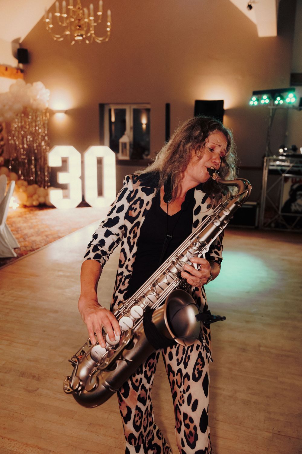 A saxophone player in a leopard print outfit performs in a dimly lit venue.