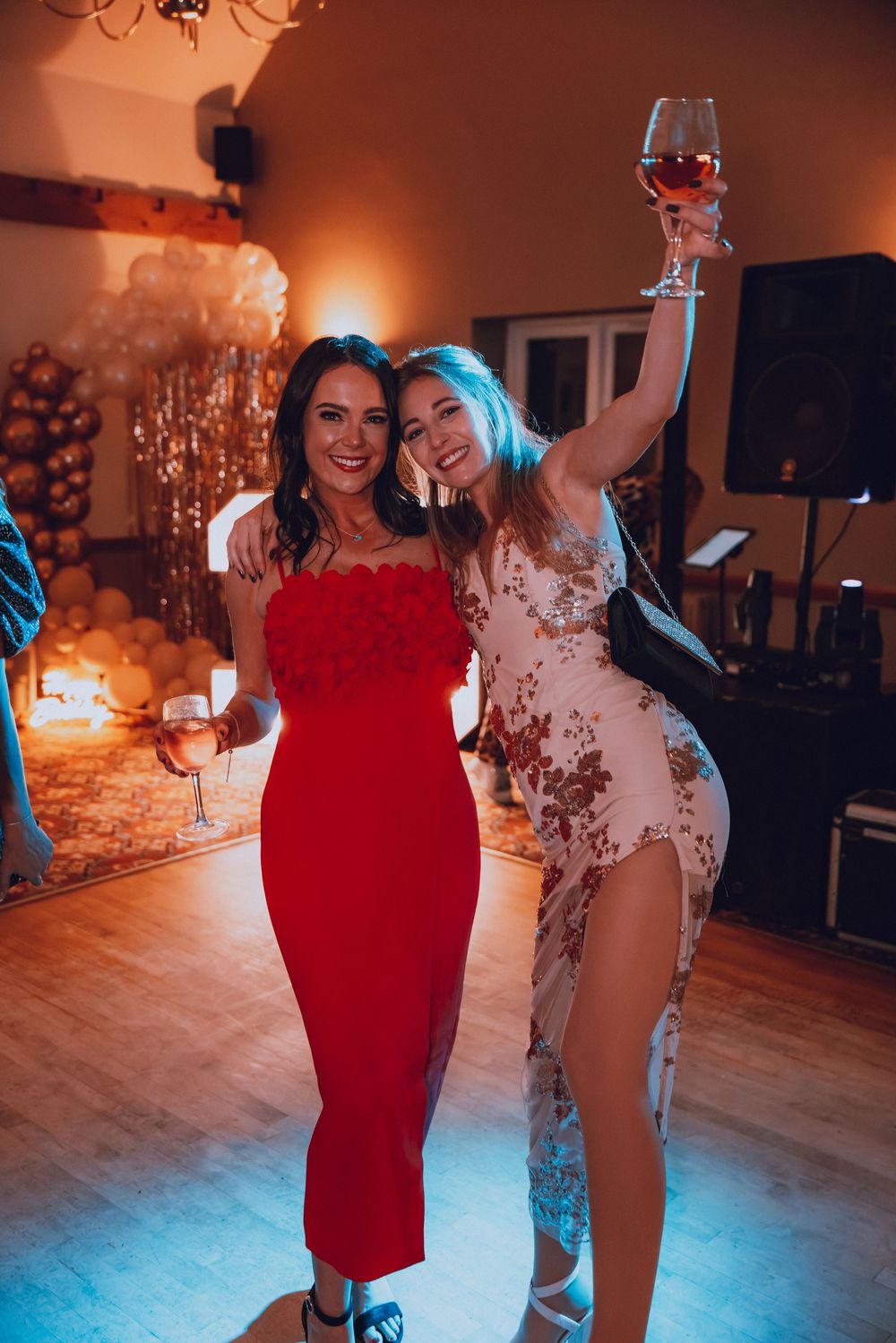 People dancing and celebrating at a party with colorful mood lighting on a wooden dance floor.
