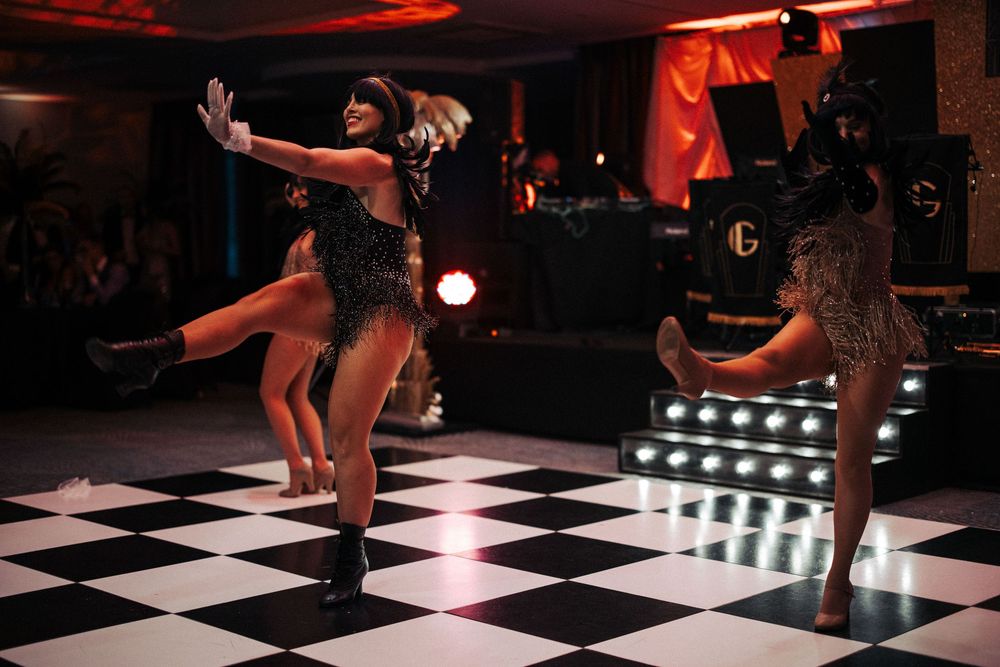 Dancers performing on a black and white checkered dance floor under red lighting.