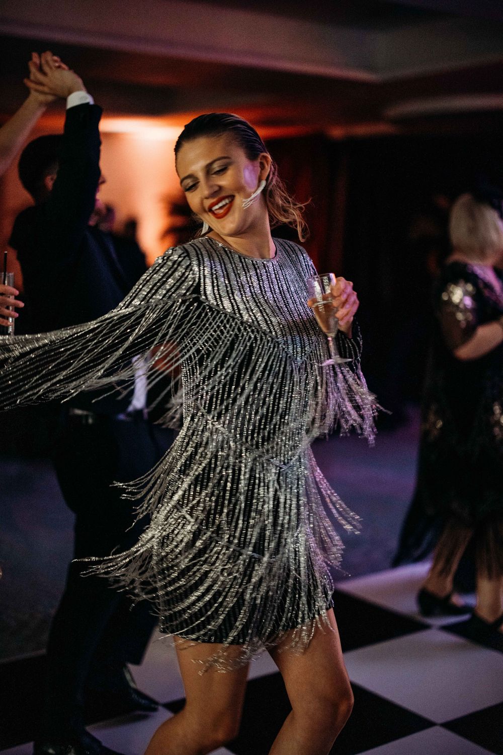 A dancer in a sparkly fringe dress twirls on a black and white checkered floor.