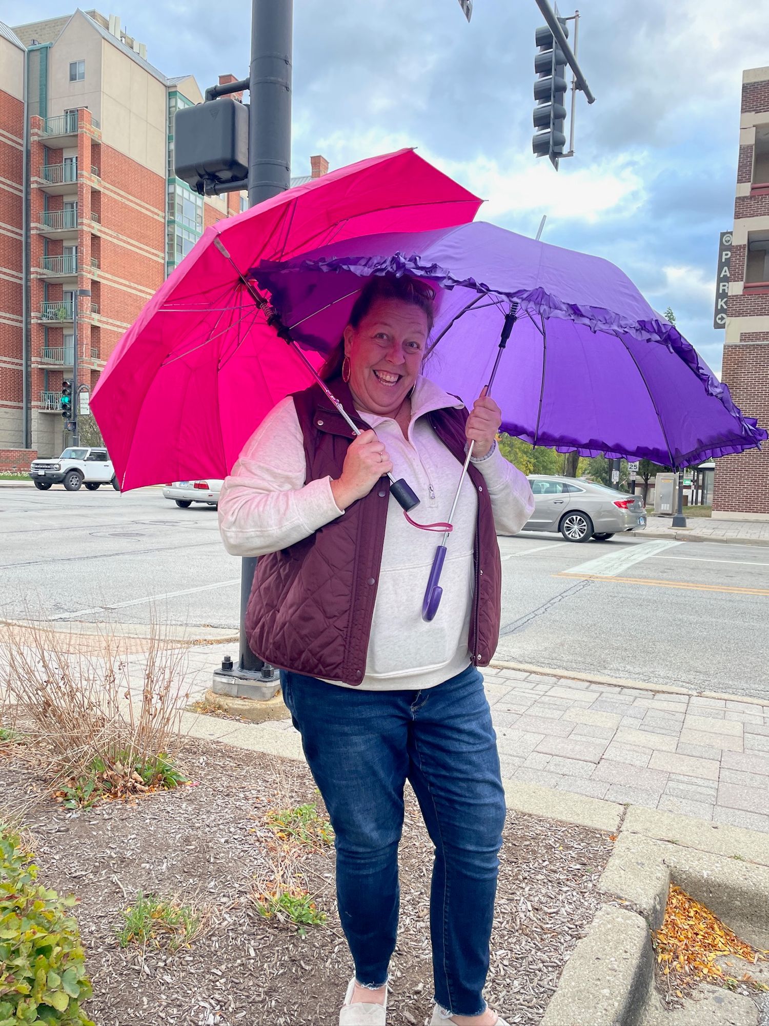 Three views of someone holding colorful pink and purple umbrellas while standing on a sidewalk near apartment buildings.