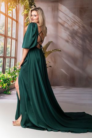 Elegant emerald green maxi dress with flowy silhouette and train photographed in sunlit studio setting.